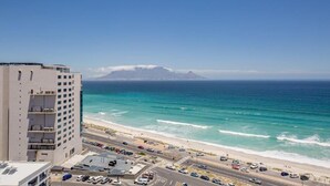 A coastal view with a beach, ocean, and a building with multiple floors and balconies. - Infinity Self-Catering Apartments (Cape Town)