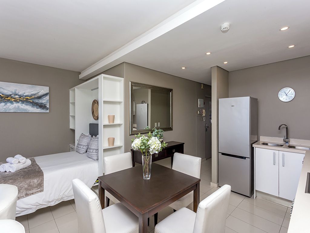 A modern hotel room with a bed, a dining area, a kitchen, and a bathroom.