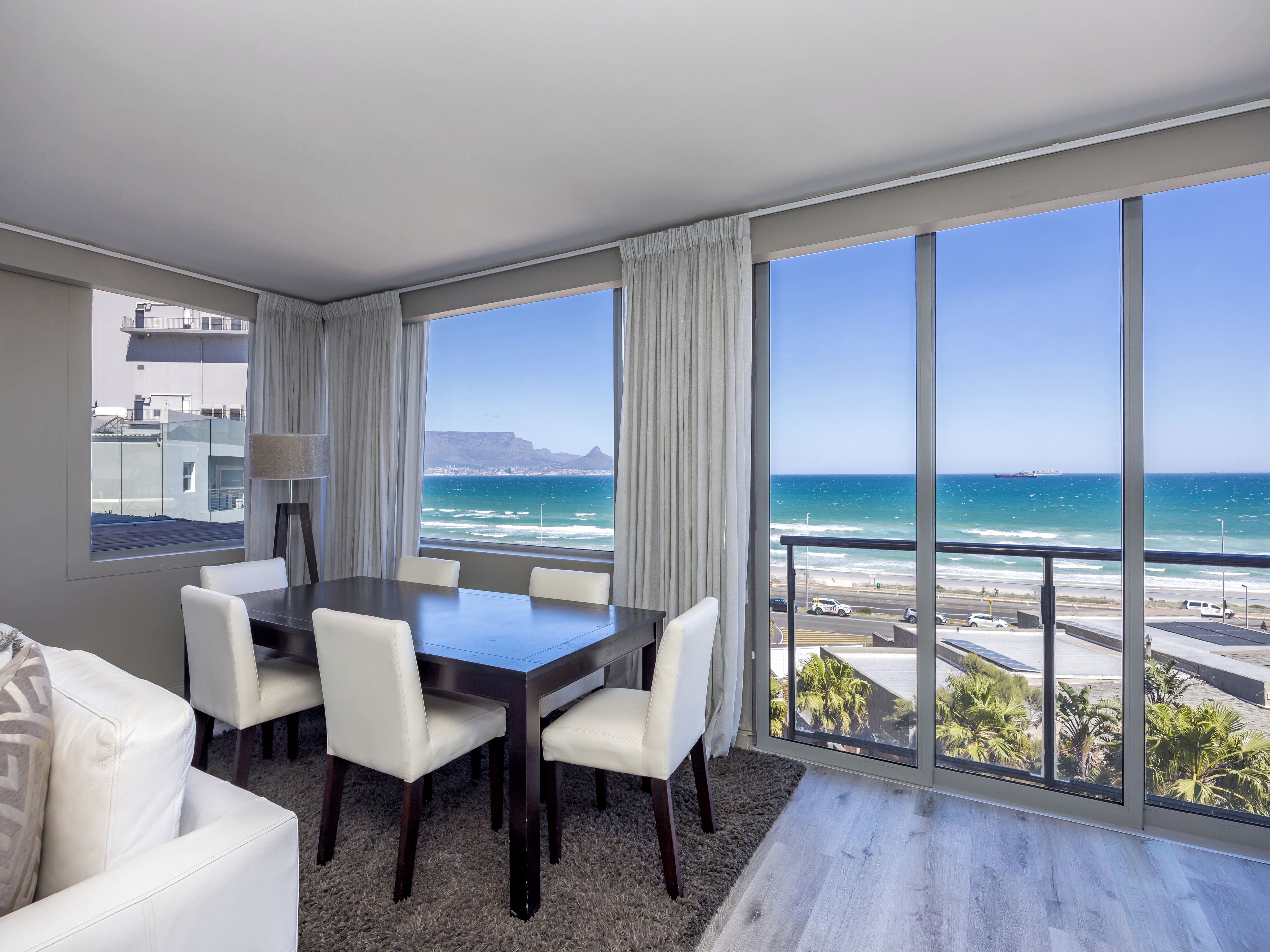 A modern room with a dining table, chairs, and a view of the ocean.