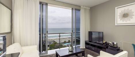 A modern living room with a large window, a flat-screen TV, and a view of the ocean.