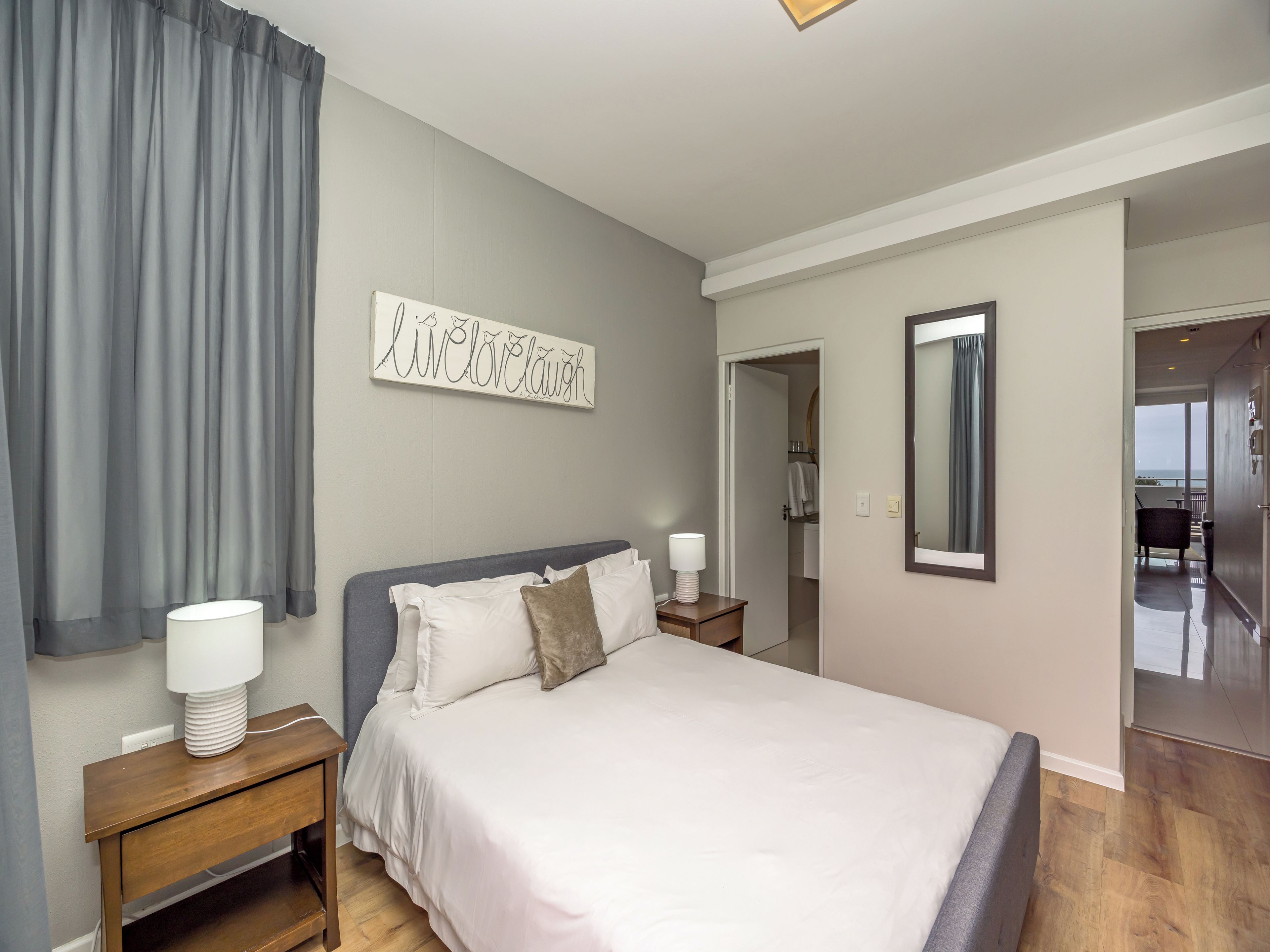 A hotel room with a bed, bedside lamps, a mirror, and a view of the balcony.