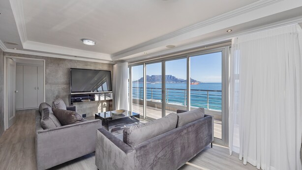 A modern living room with a large flat-screen TV, grey sofas, and a coffee table. - Infinity Self-Catering Apartments (Cape Town)