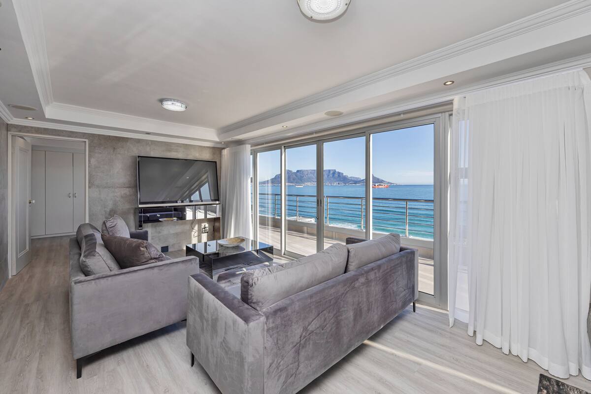 A modern living room with a large flat-screen TV, grey sofas, and a coffee table.