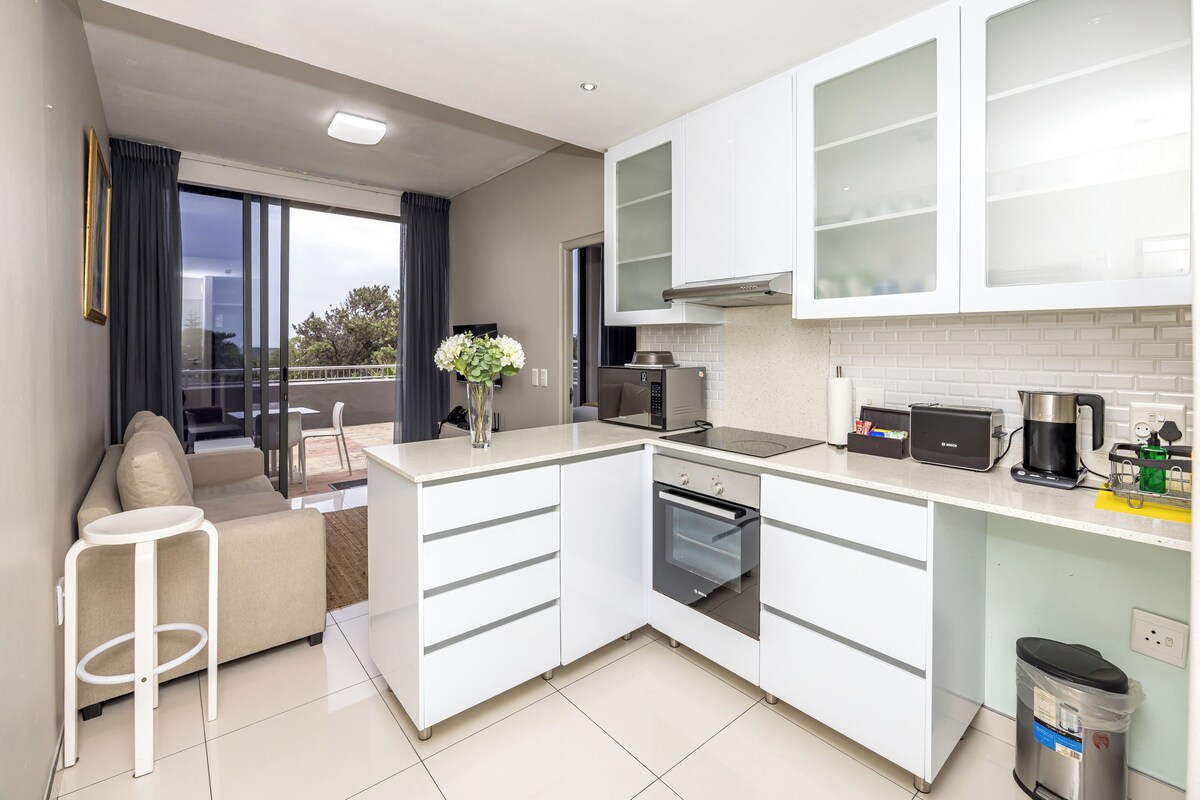 A modern kitchen with white cabinetry, a built-in oven, and a coffee maker.