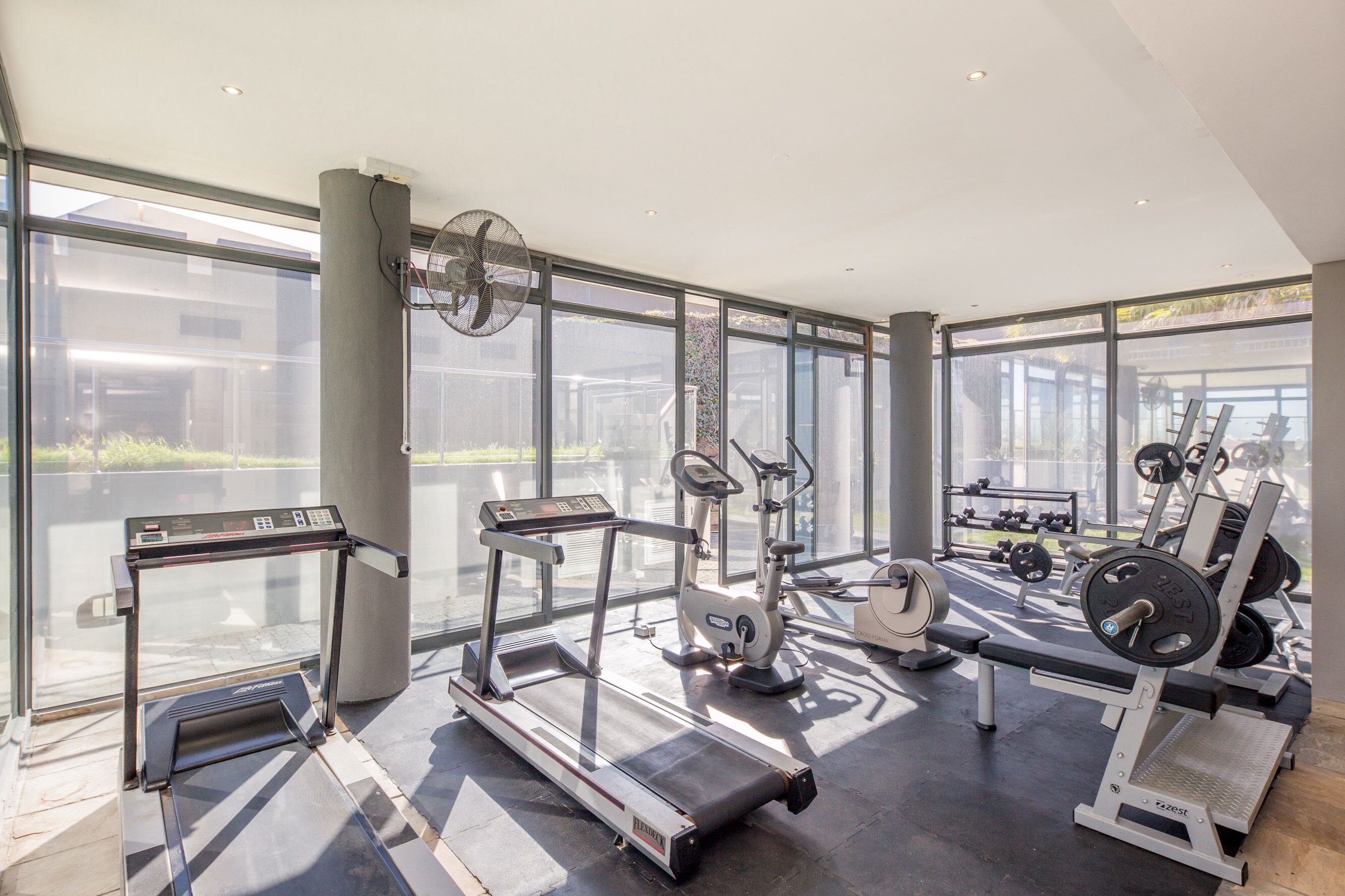 A modern gym with cardio equipment, weight machines, and a large window providing natural light.