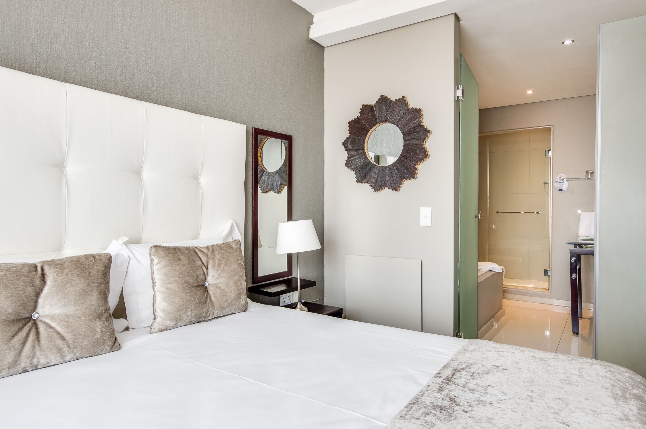 Hotelkamer met een groot bed, nachtkastje met lamp, spiegel en douche.
