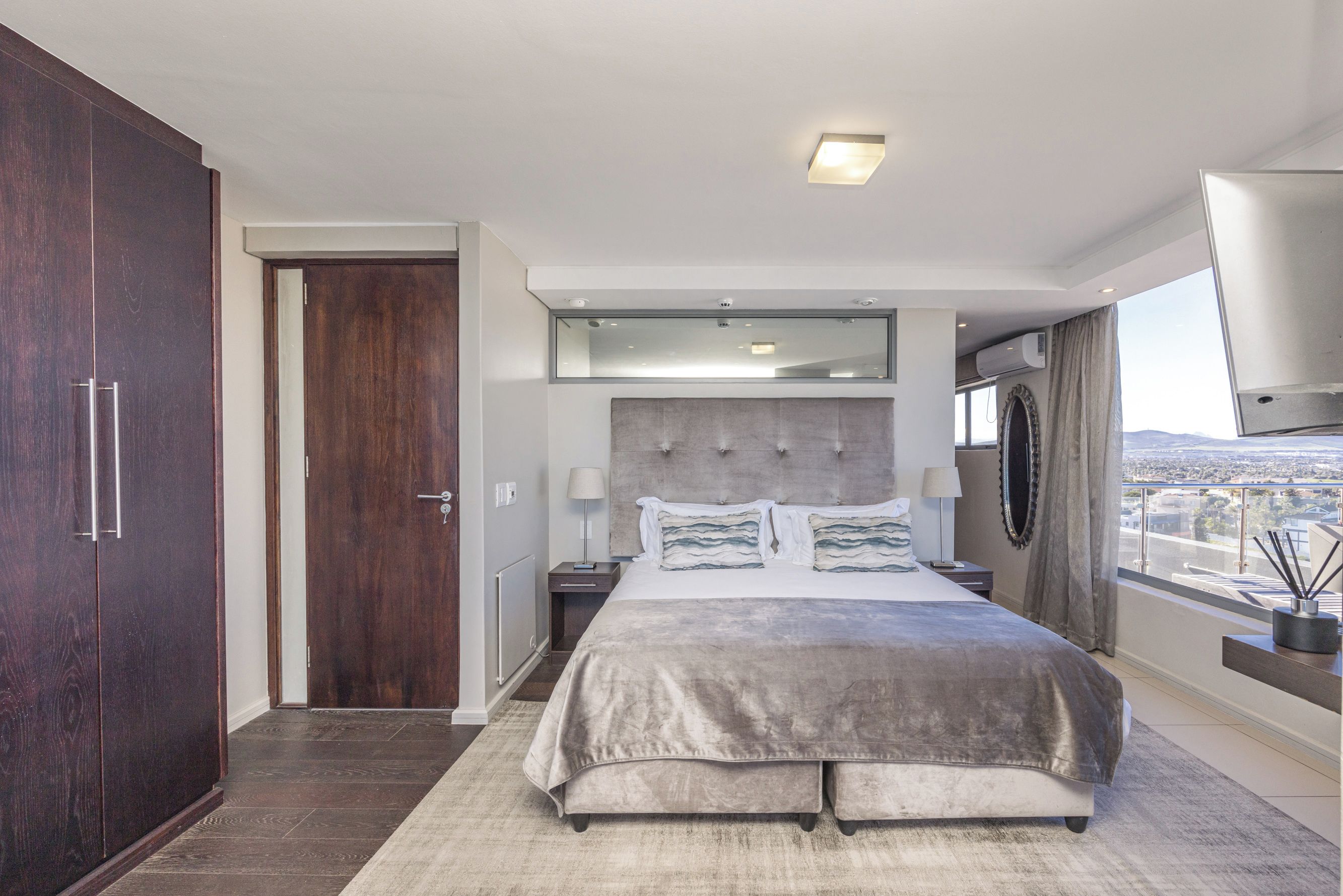 Ein modernes Hotelzimmer mit einem großen Bett, einem Kleiderschrank, einem Spiegel und Blick auf die Stadt.