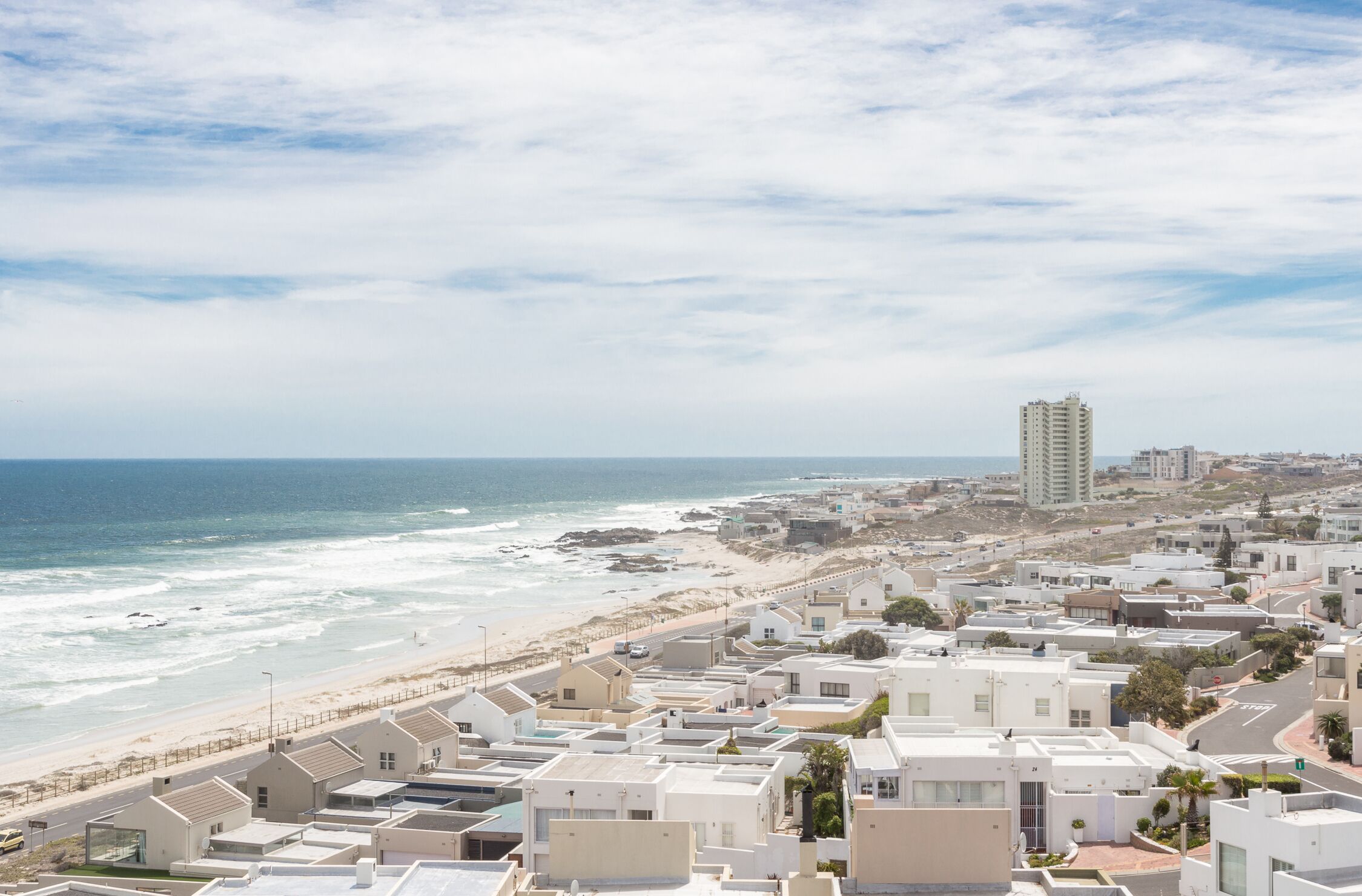 A coastal residential area with modern buildings, a beach, and a clear sky.