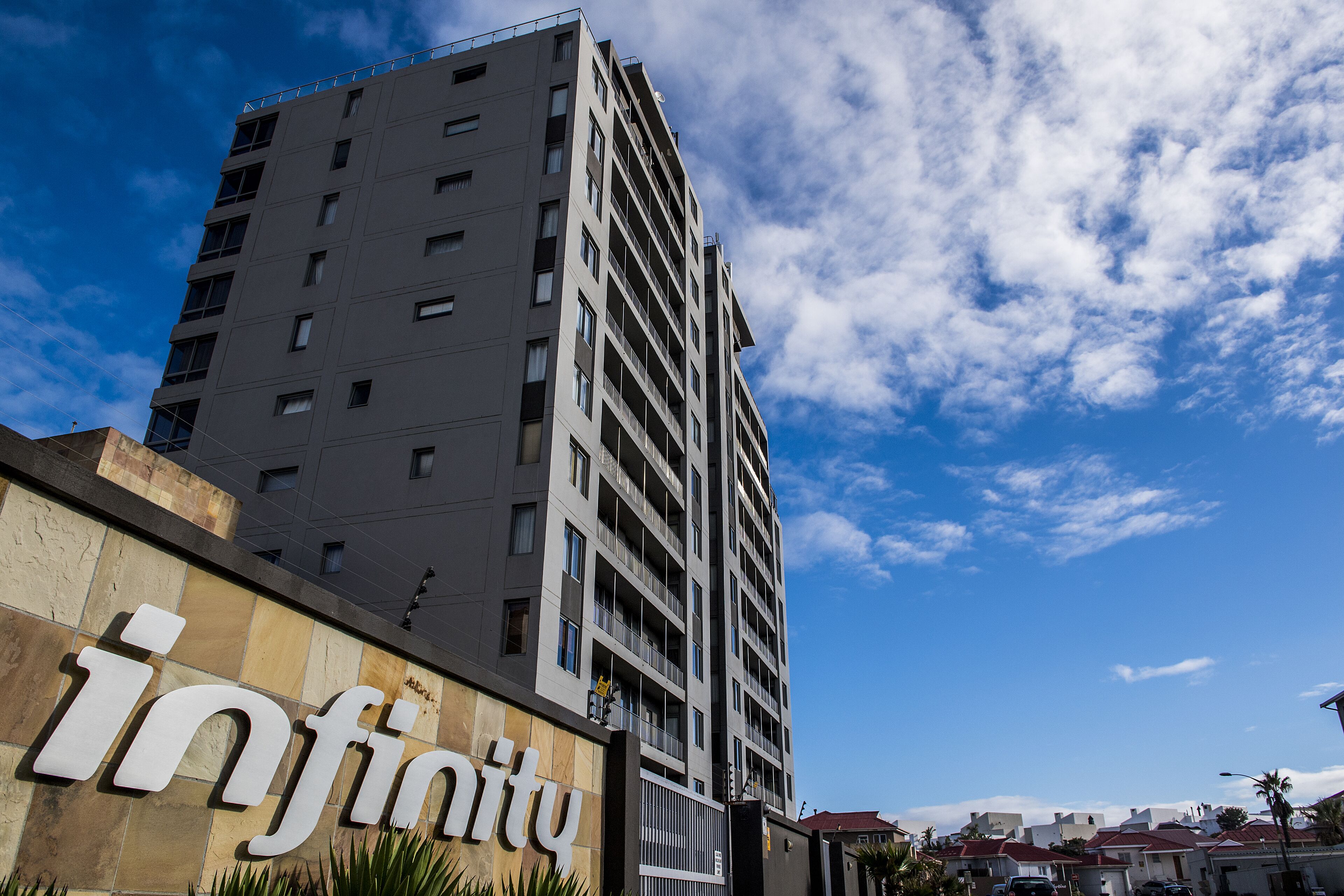 A modern high-rise building with a prominent 'infinity' sign on the lower facade, featuring multiple balconies and a clear sky in the background.
