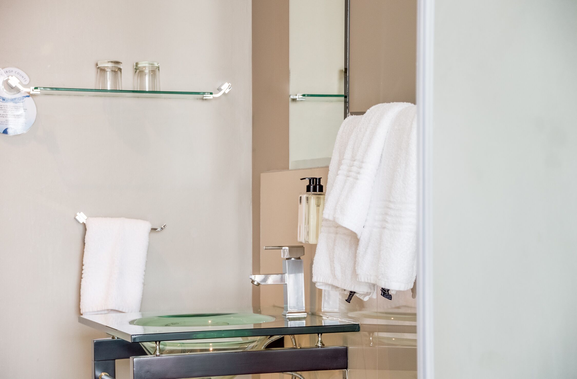 A bathroom with a glass sink, a mirror, and two shelves with toiletries.