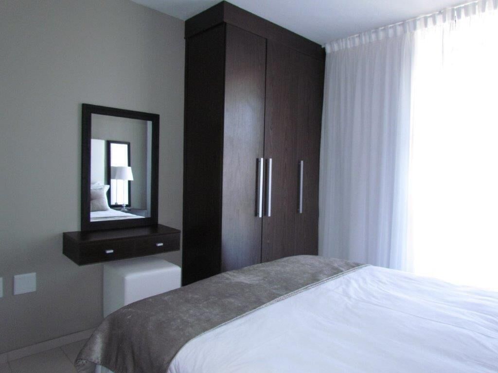 Un dormitorio con una cama, un armario de madera oscura, un espejo y una ventana con cortinas.