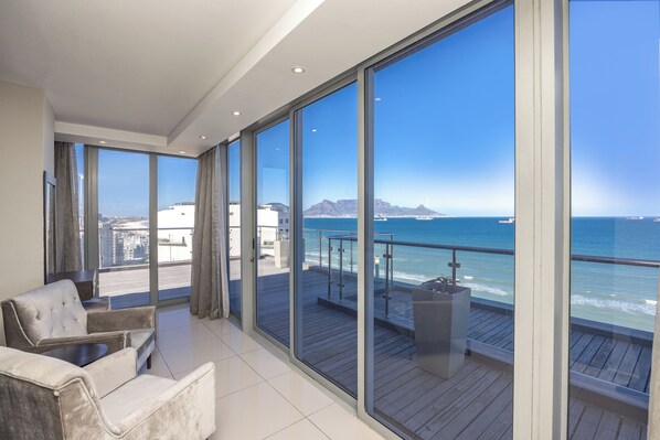 A modern living room with a large balcony overlooking a coastal view. - Infinity Apartments (Cape Town)