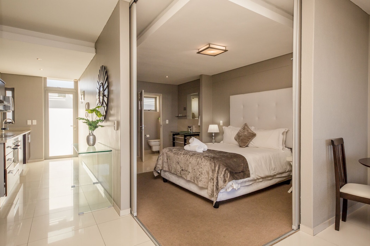 A modern bedroom with a large bed, a glass partition, a bedside table, and a chair.