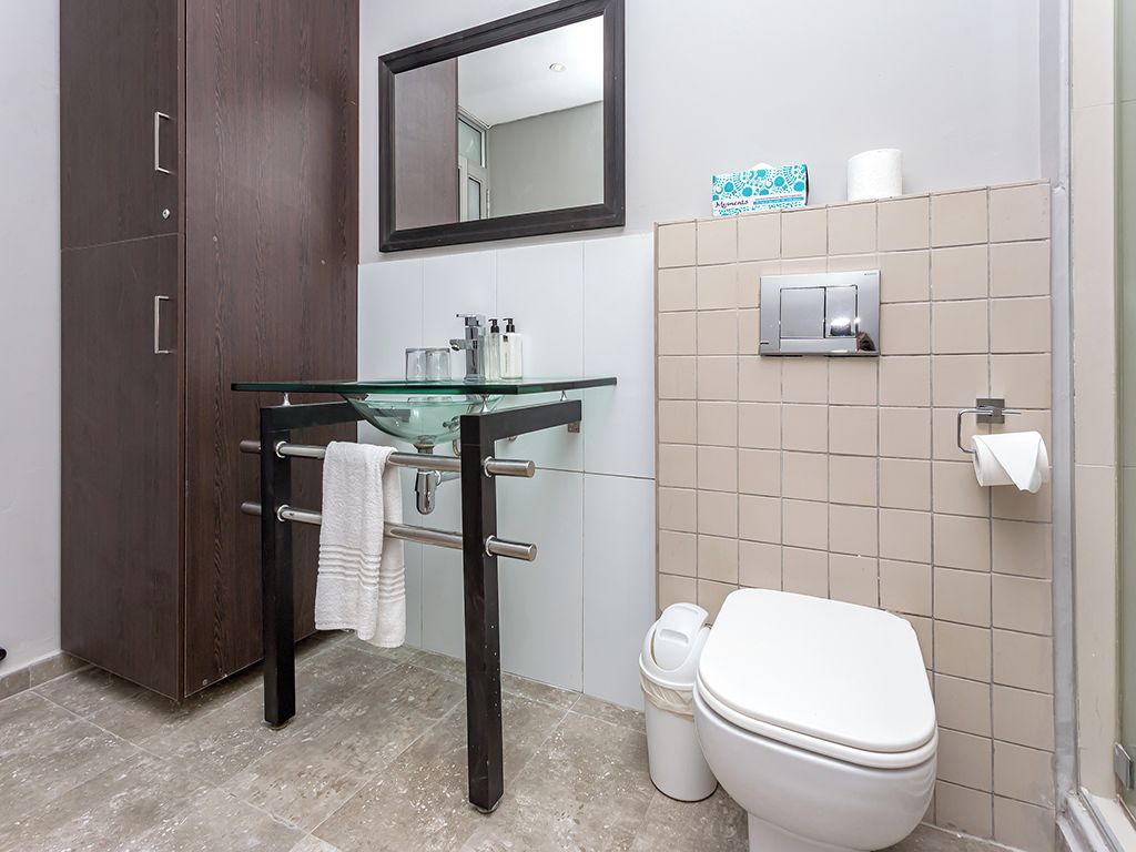 A bathroom with a glass sink, dark wooden cabinet, white toilet, and beige tiled walls.
