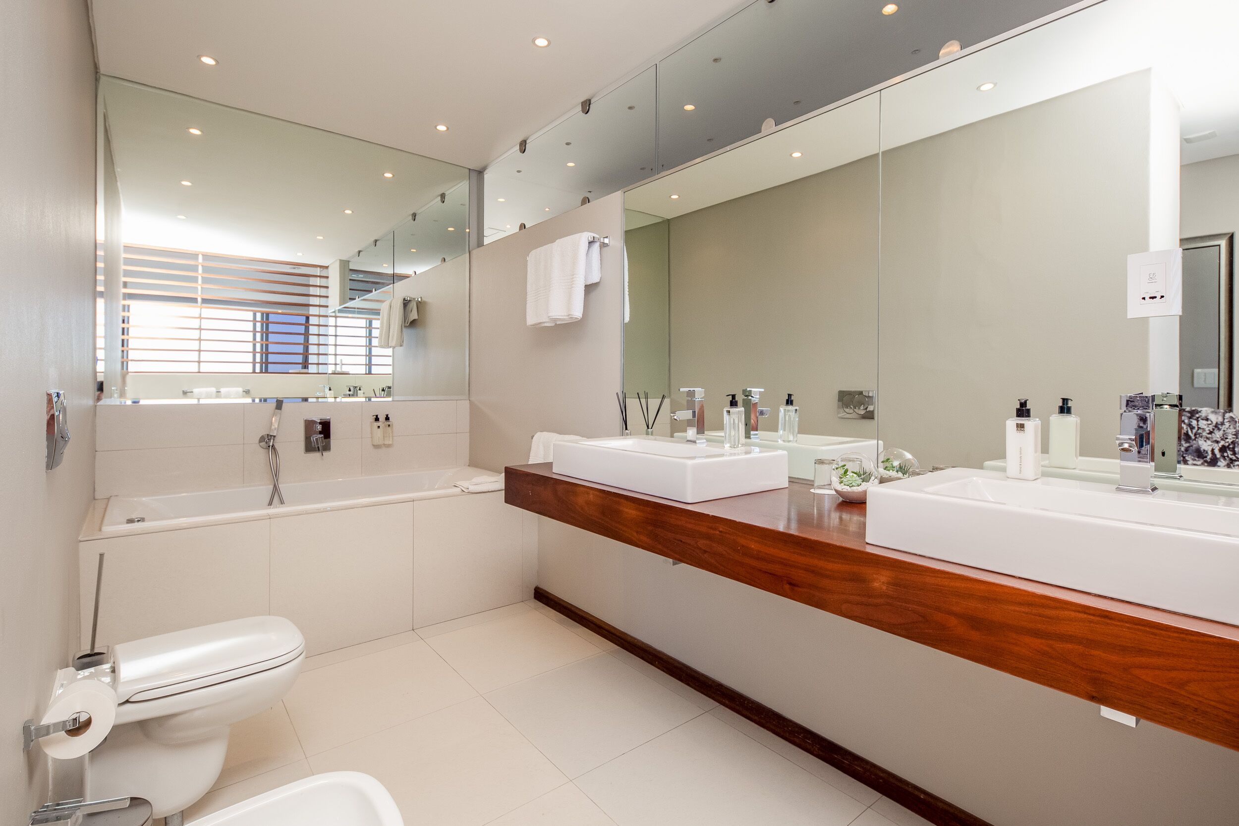 Un baño moderno con un espejo grande, dos lavamanos, una bañera y un inodoro.