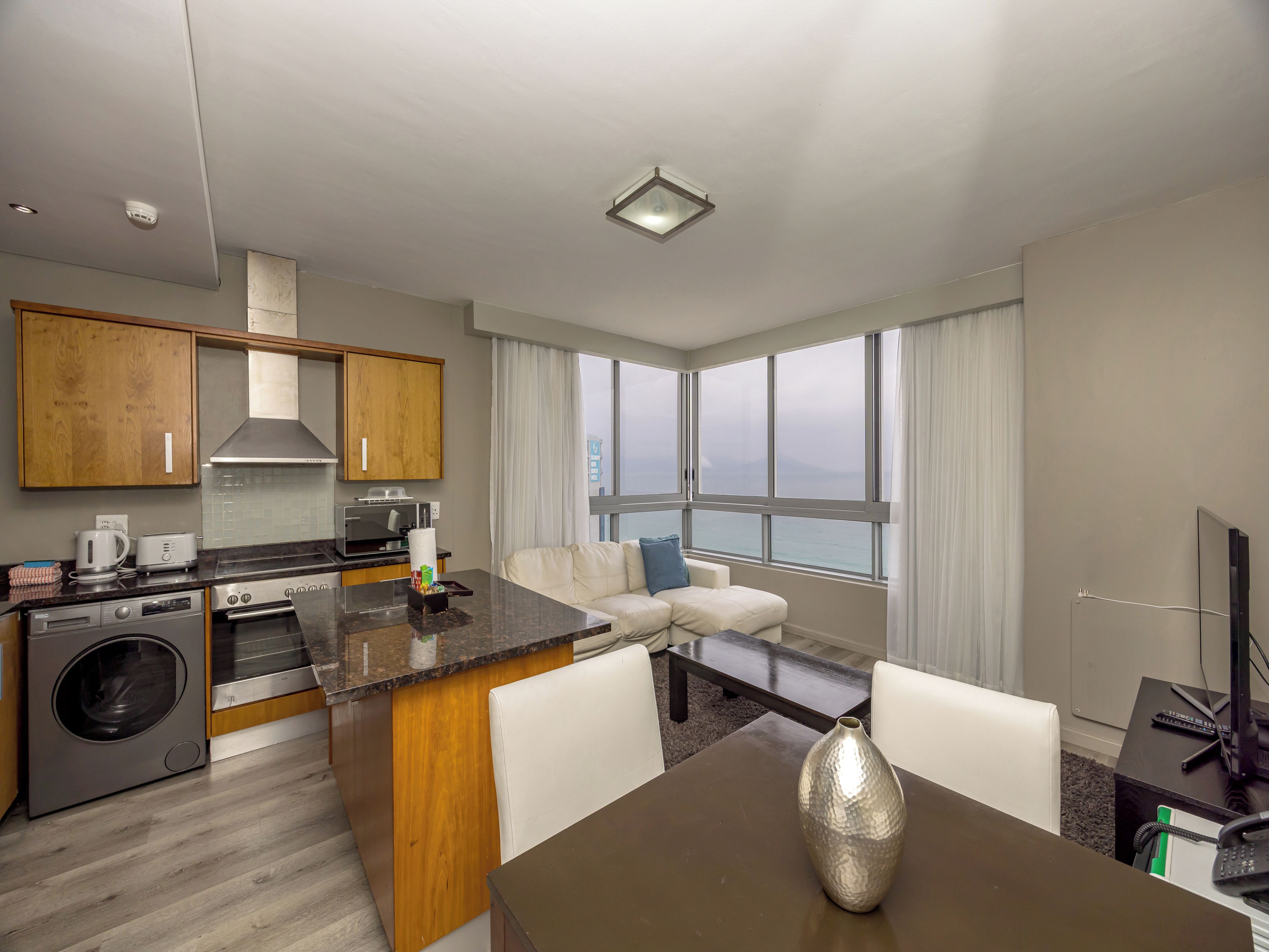 A modern hotel room with a kitchen, a dining area, and a seating area with a view.