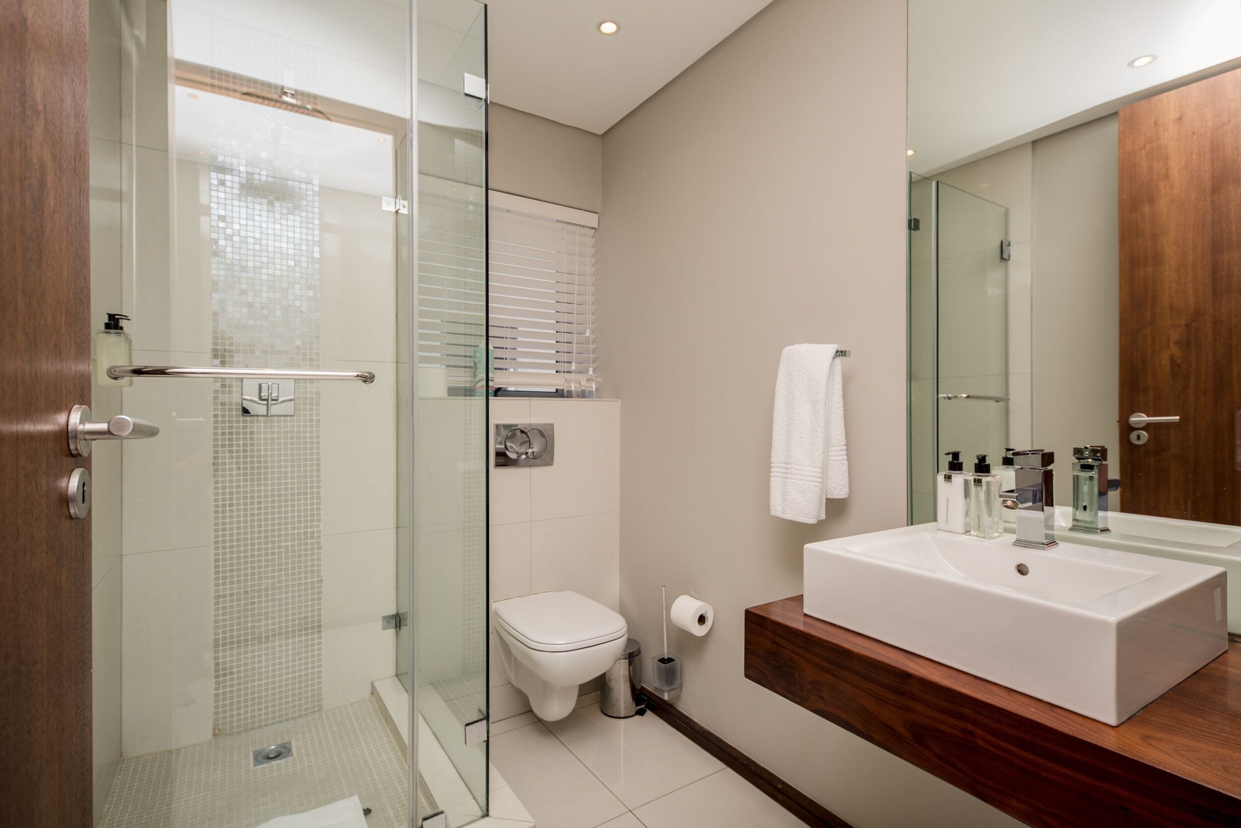 A modern bathroom with a glass shower enclosure, a white toilet, and a large rectangular sink with a wooden vanity.