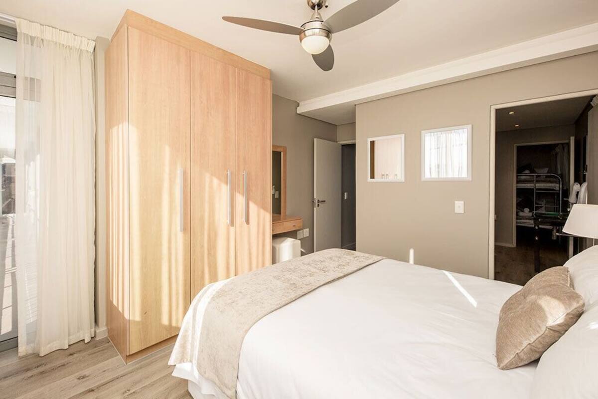 A bedroom with a bed, a wardrobe, a ceiling fan, and a view of a balcony.