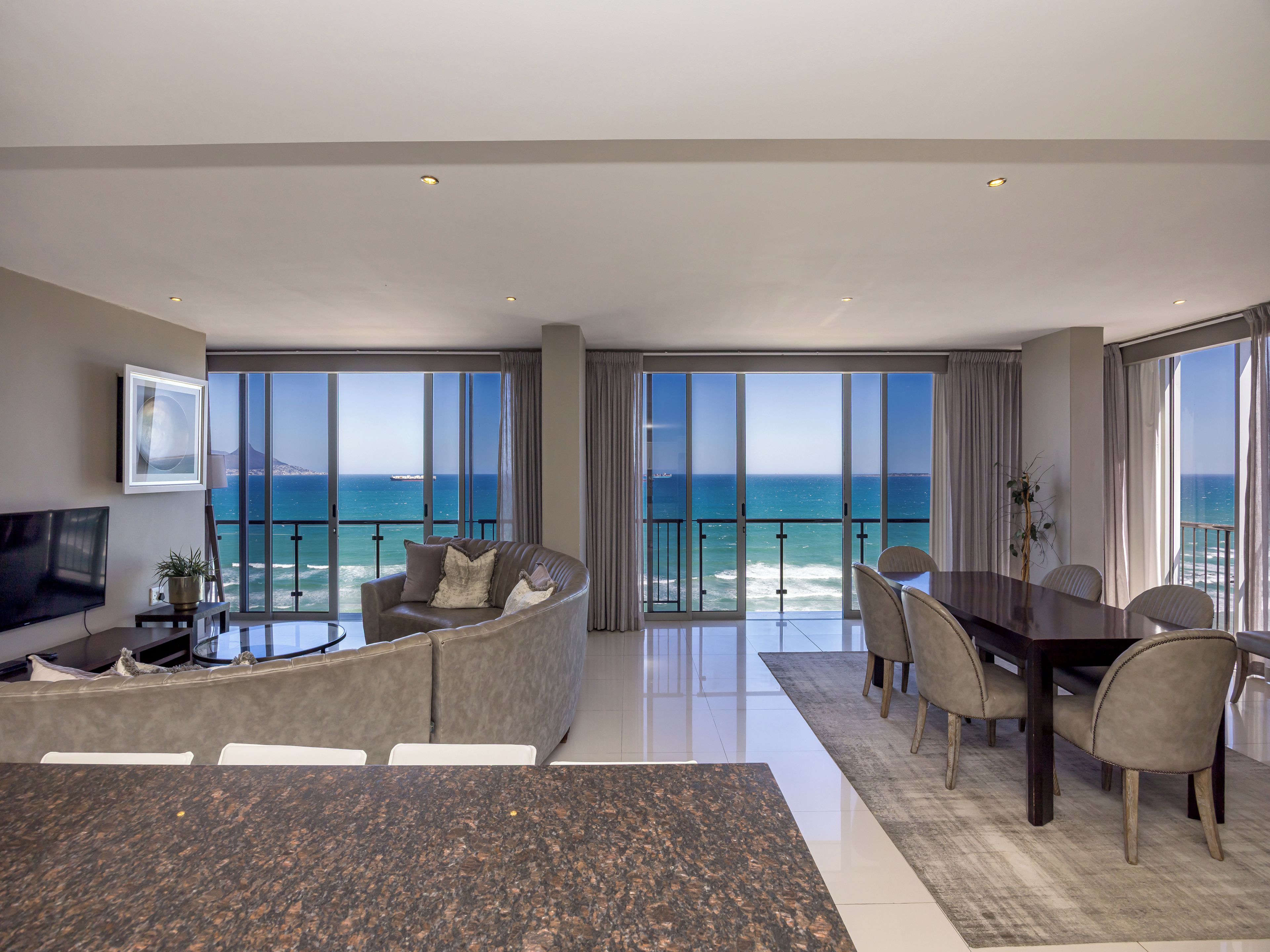 A modern living room with a large window, a flat-screen TV, a sofa, and a dining area with chairs and a table.
