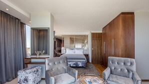 A modern hotel room with a large bed, two armchairs, a wooden wardrobe, and a view of the city through large windows. - Infinity Self-Catering Apartments (Cape Town)