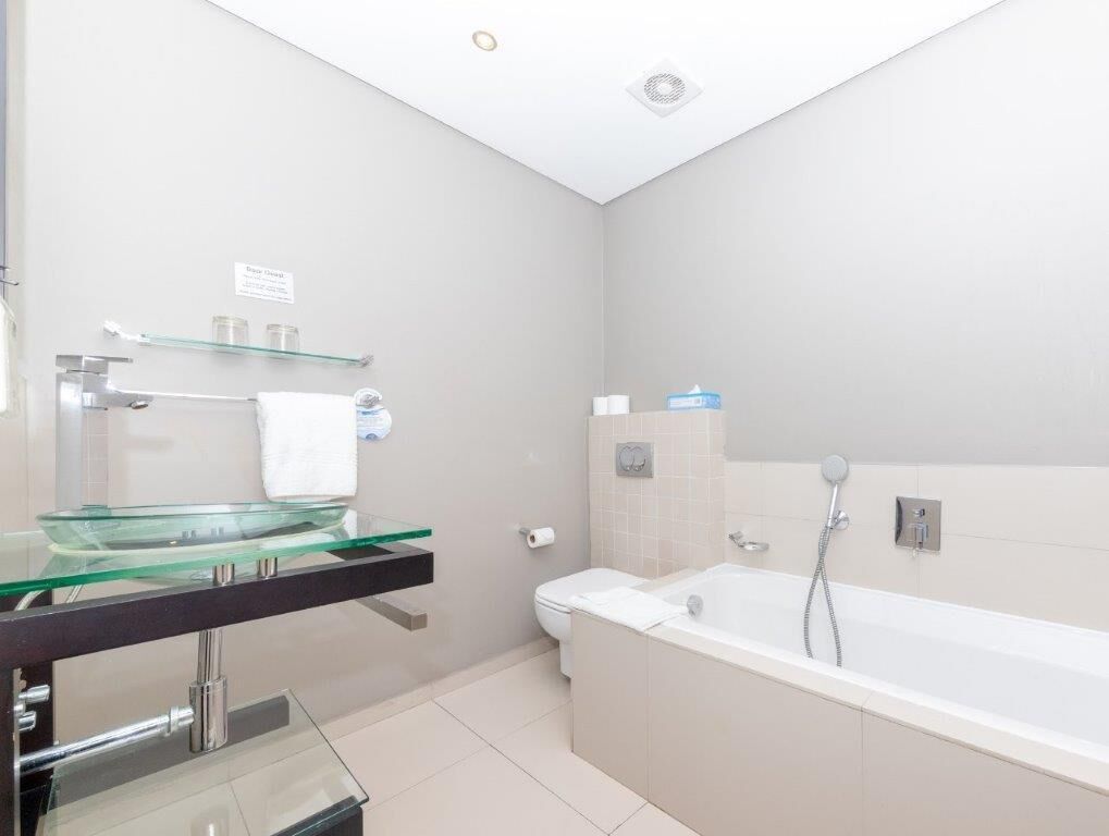Een moderne badkamer met een glazen wastafel, een wit toilet en een bad.