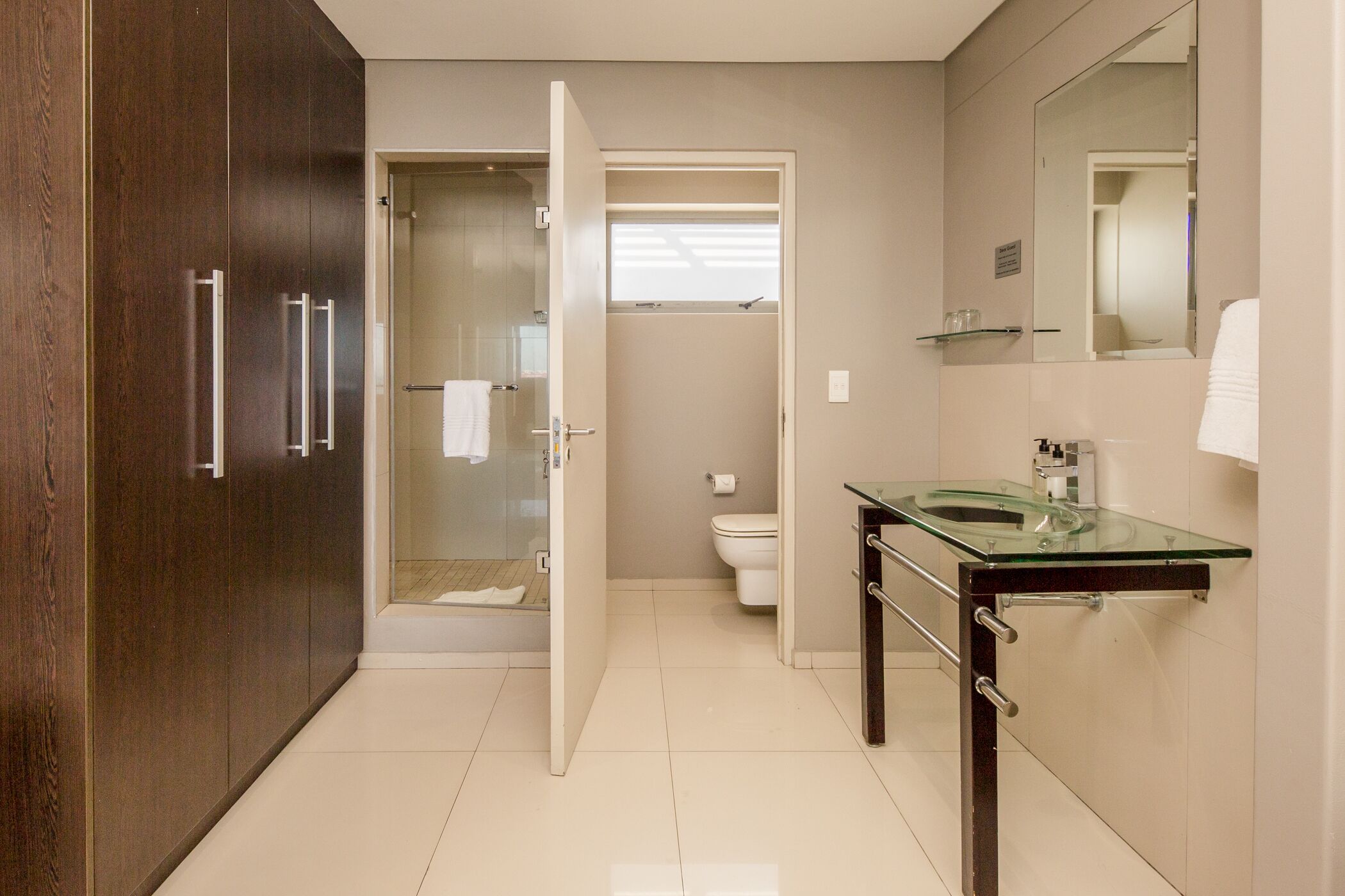 A modern bathroom with a glass shower enclosure, a glass sink, and a large mirror.