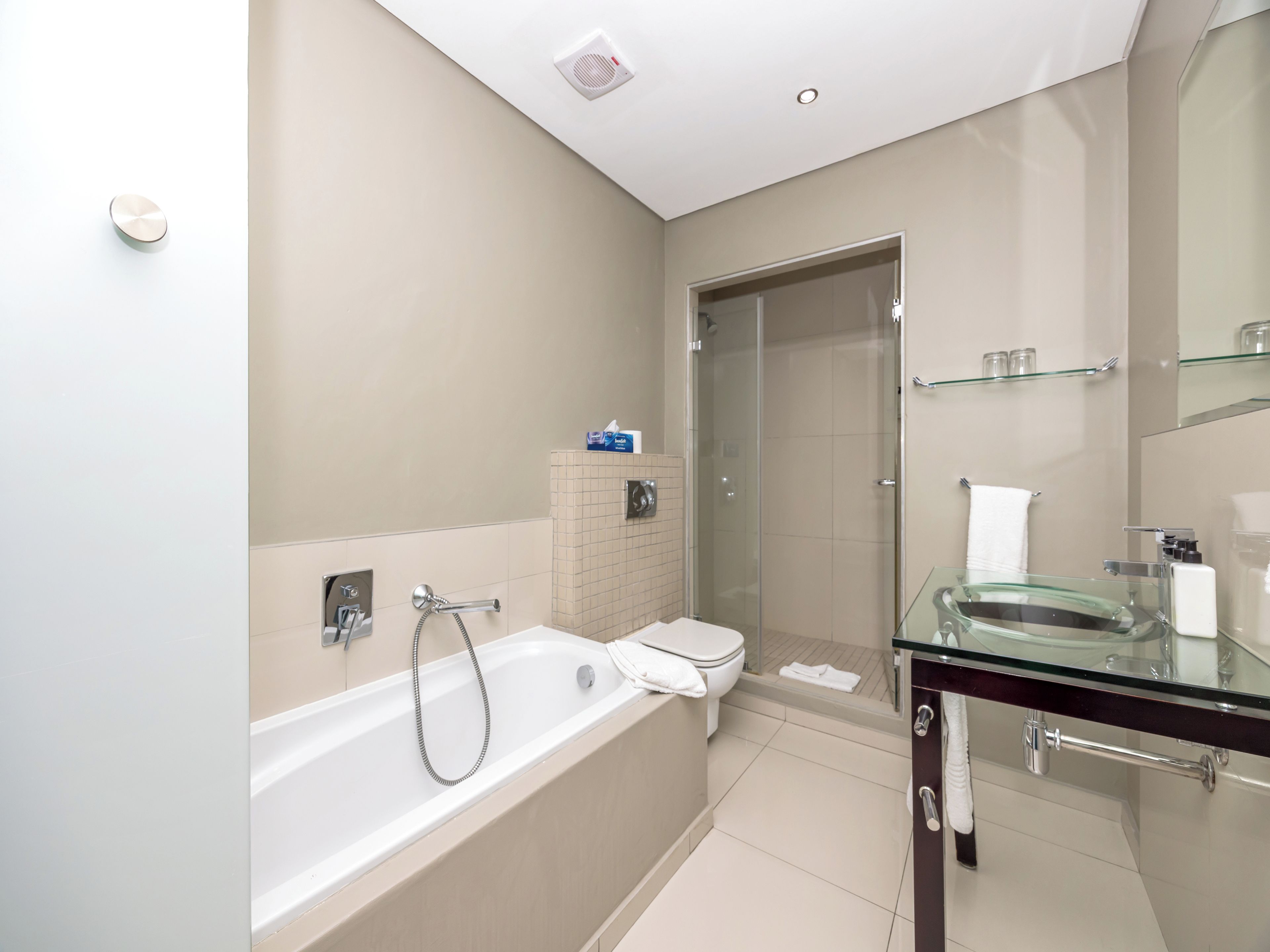 A modern bathroom with a bathtub, toilet, and glass shower enclosure.