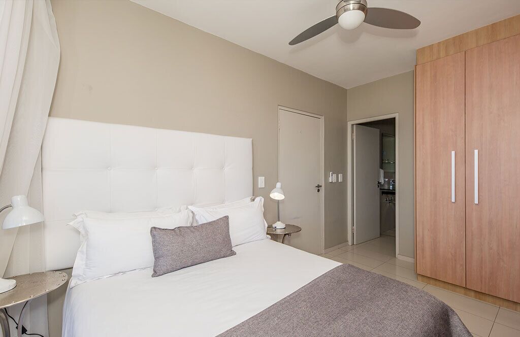 Une chambre à coucher avec un grand lit, un ventilateur de plafond, une armoire en bois et une porte donnant sur une salle de bain.