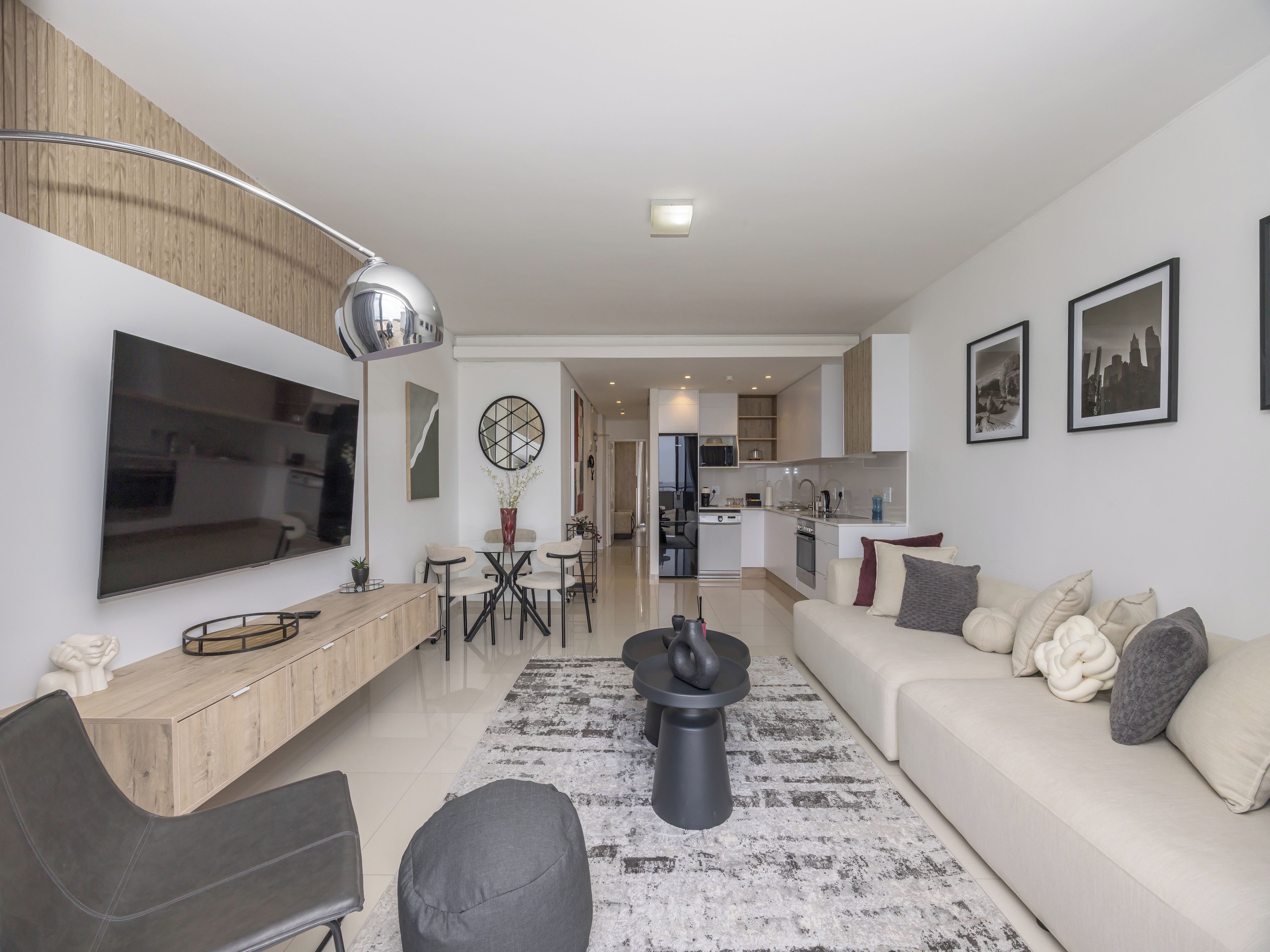 A modern living room with a flat-screen TV, a sofa, a coffee table, and a dining area with chairs and a small table.