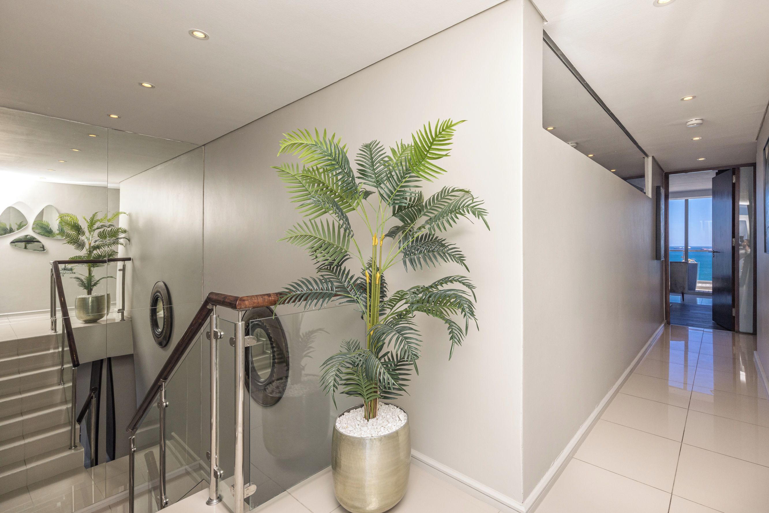 Un intérieur moderne avec un escalier, une plante en pot et une vue sur la mer.