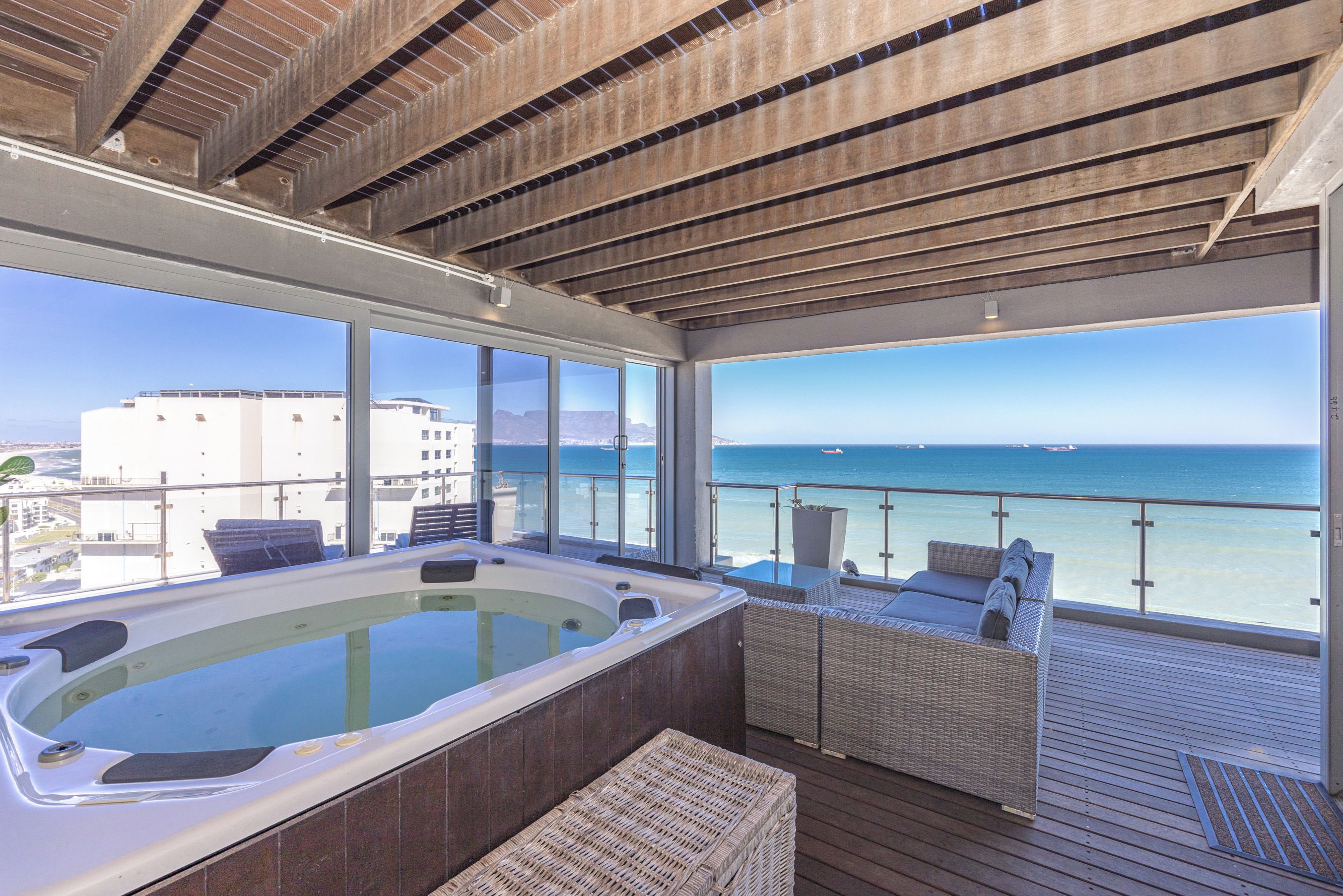 A rooftop terrace with a hot tub, wicker furniture, and a view of the sea.