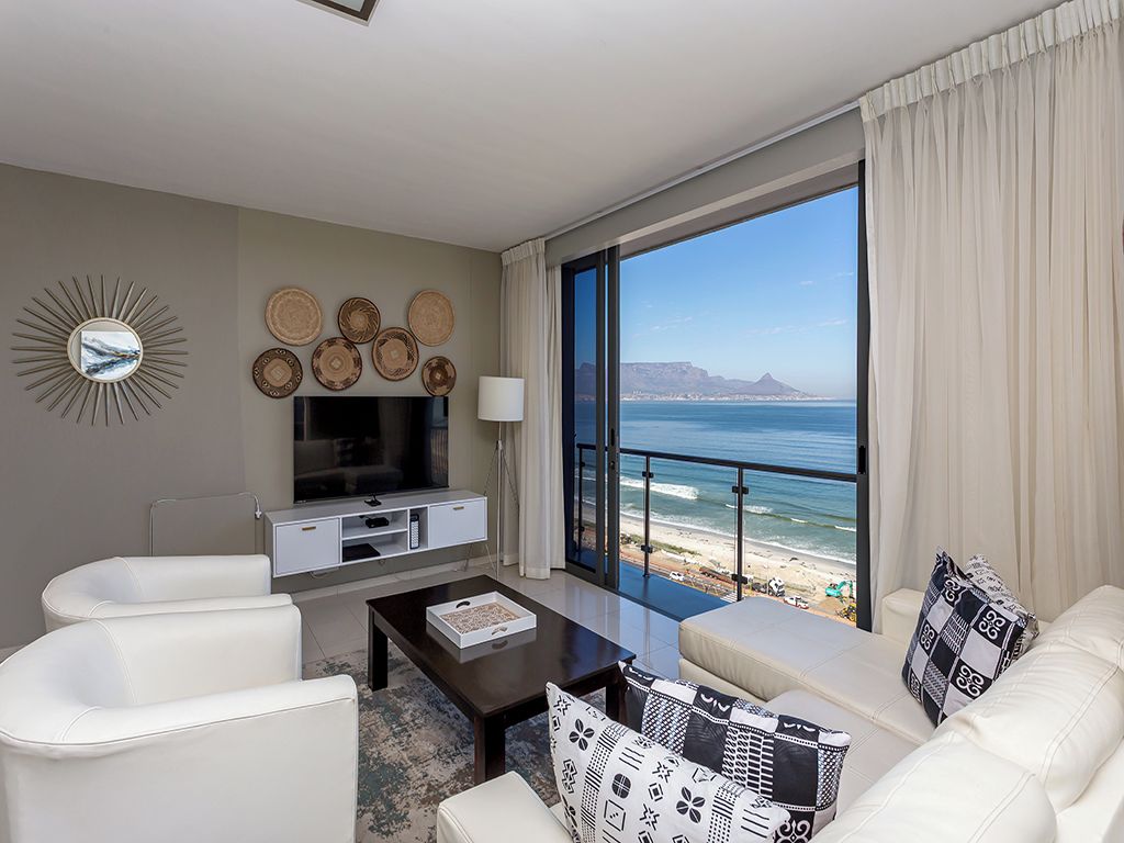 Una sala de estar moderna con un gran ventanal con vista a la playa, un televisor de pantalla plana y una zona de estar con una mesa de centro.