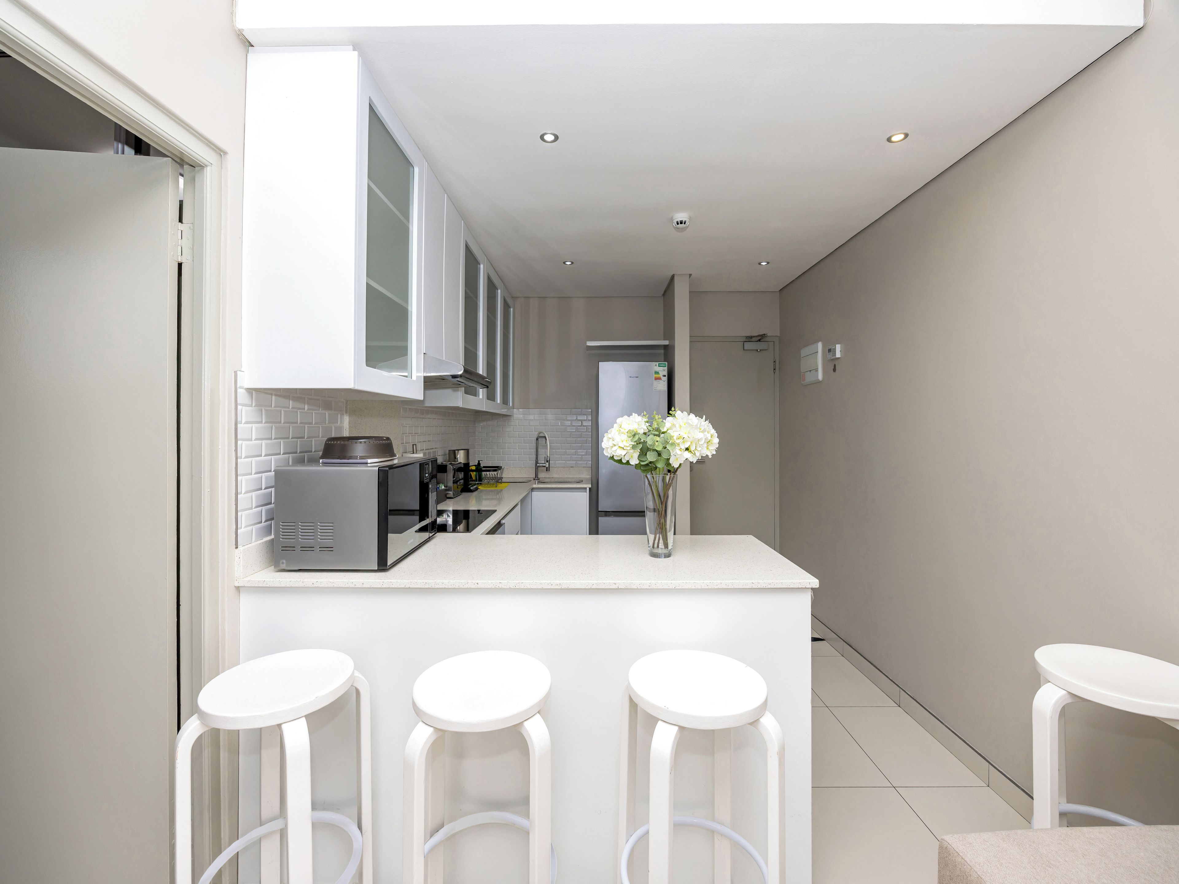 A modern kitchen with white cabinetry, a central island with stools, and a refrigerator.