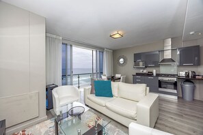 A modern living room with a glass coffee table, a sofa, and a view of the ocean. - Infinity Apartments (Cape Town)