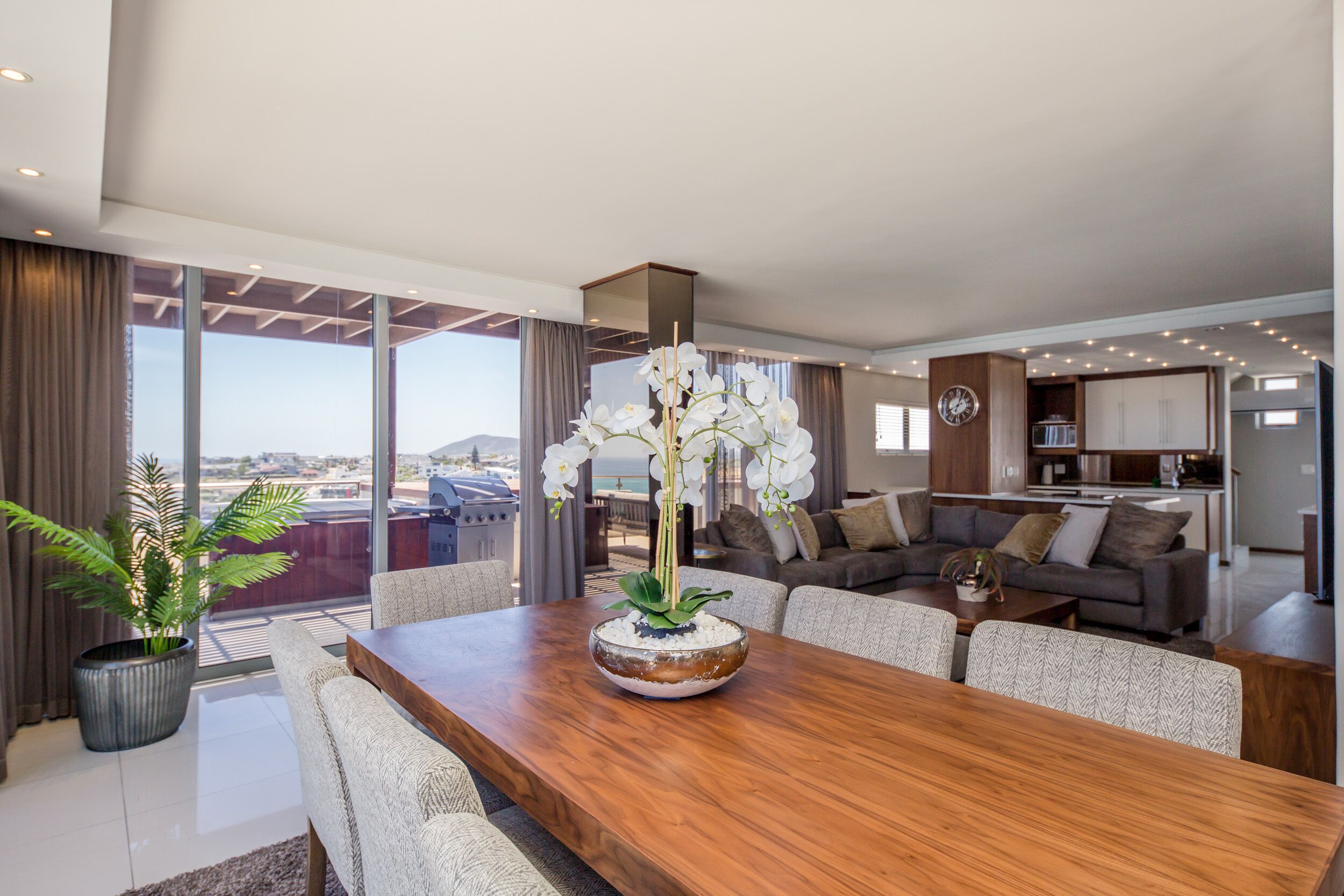 A modern living room with a wooden dining table, a sofa set, and a large window offering a view of the city.