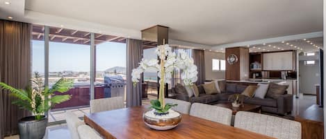 A modern living room with a wooden dining table, a sofa set, and a large window offering a view of the city.