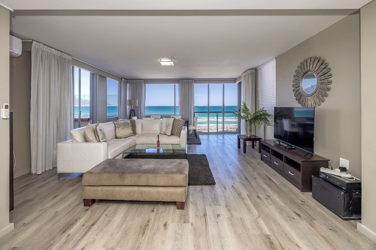 A spacious living room with a large sectional sofa, a flat-screen TV, and a view of the ocean.