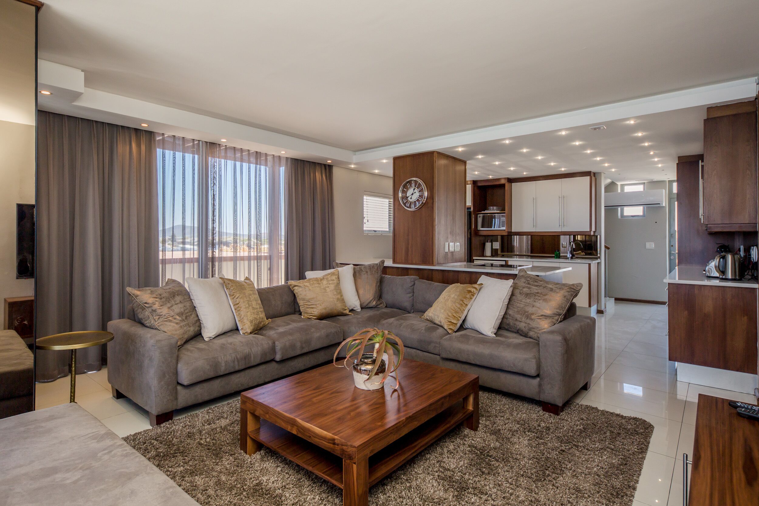 A modern living room with a sectional sofa, a wooden coffee table, and a kitchen in the background.