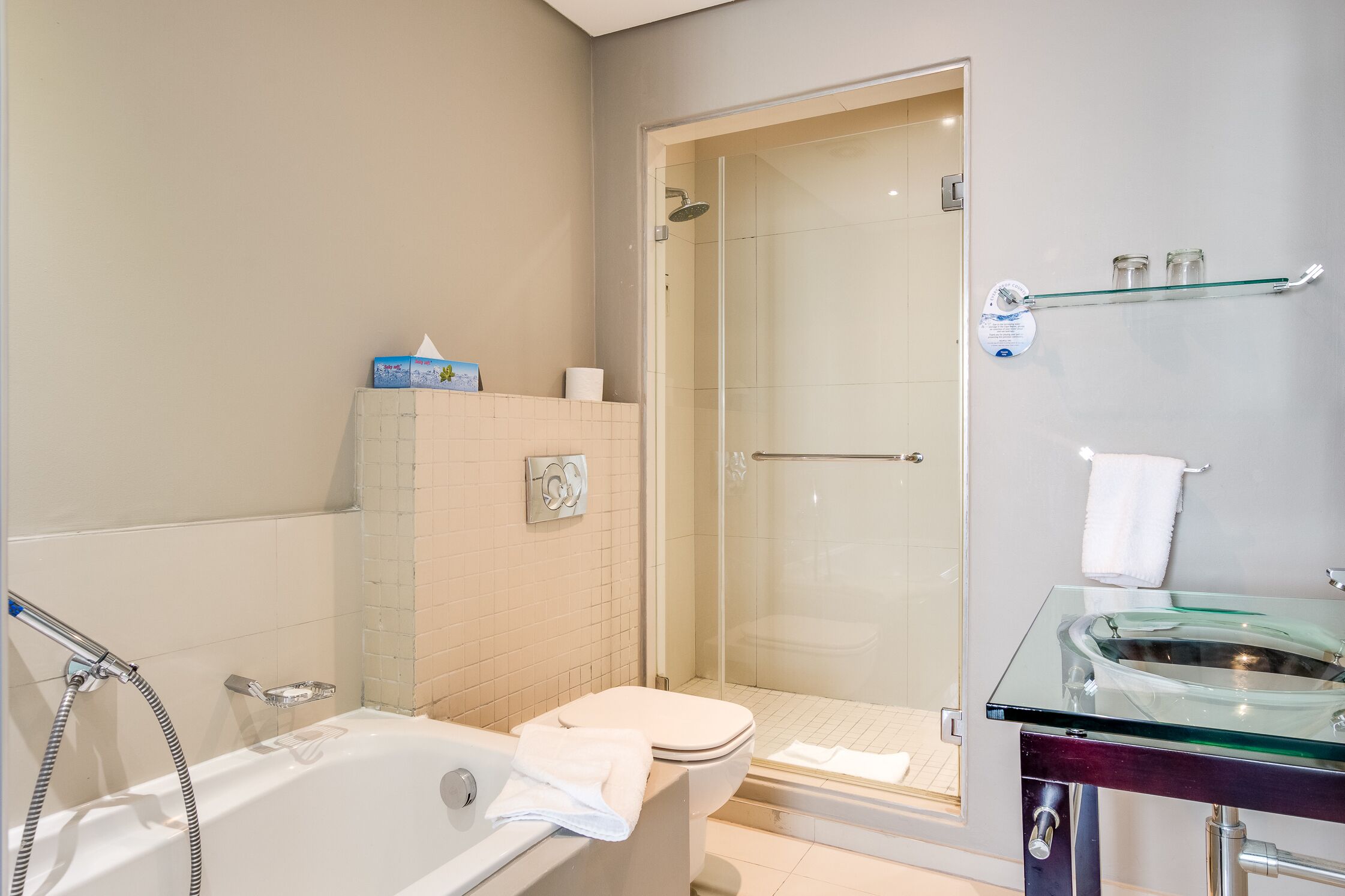 A modern bathroom with a glass-enclosed shower, a glass sink, and a bathtub.