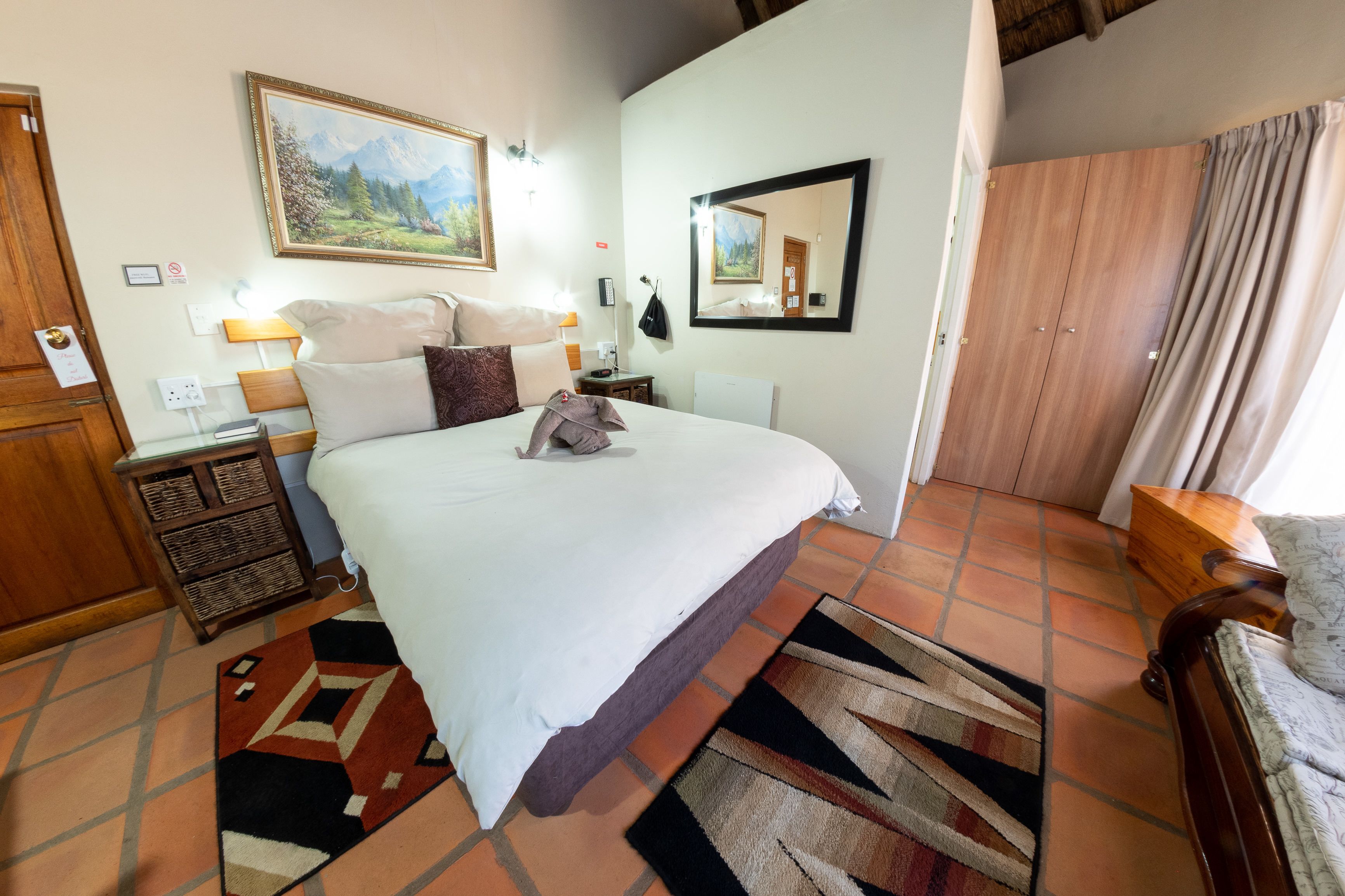 Une chambre à coucher comprenant un lit, une table de chevet, une commode, un miroir et une fenêtre avec des rideaux.