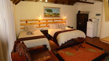 A hotel room with two beds, a wooden headboard, a painting of a tree, a small refrigerator, and a wooden bench.