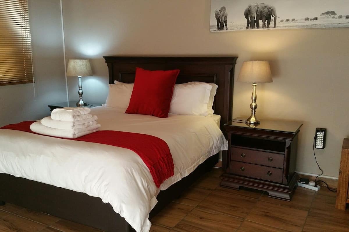 A neatly made bed with white and red bedding, two bedside tables with lamps, and a wooden nightstand.