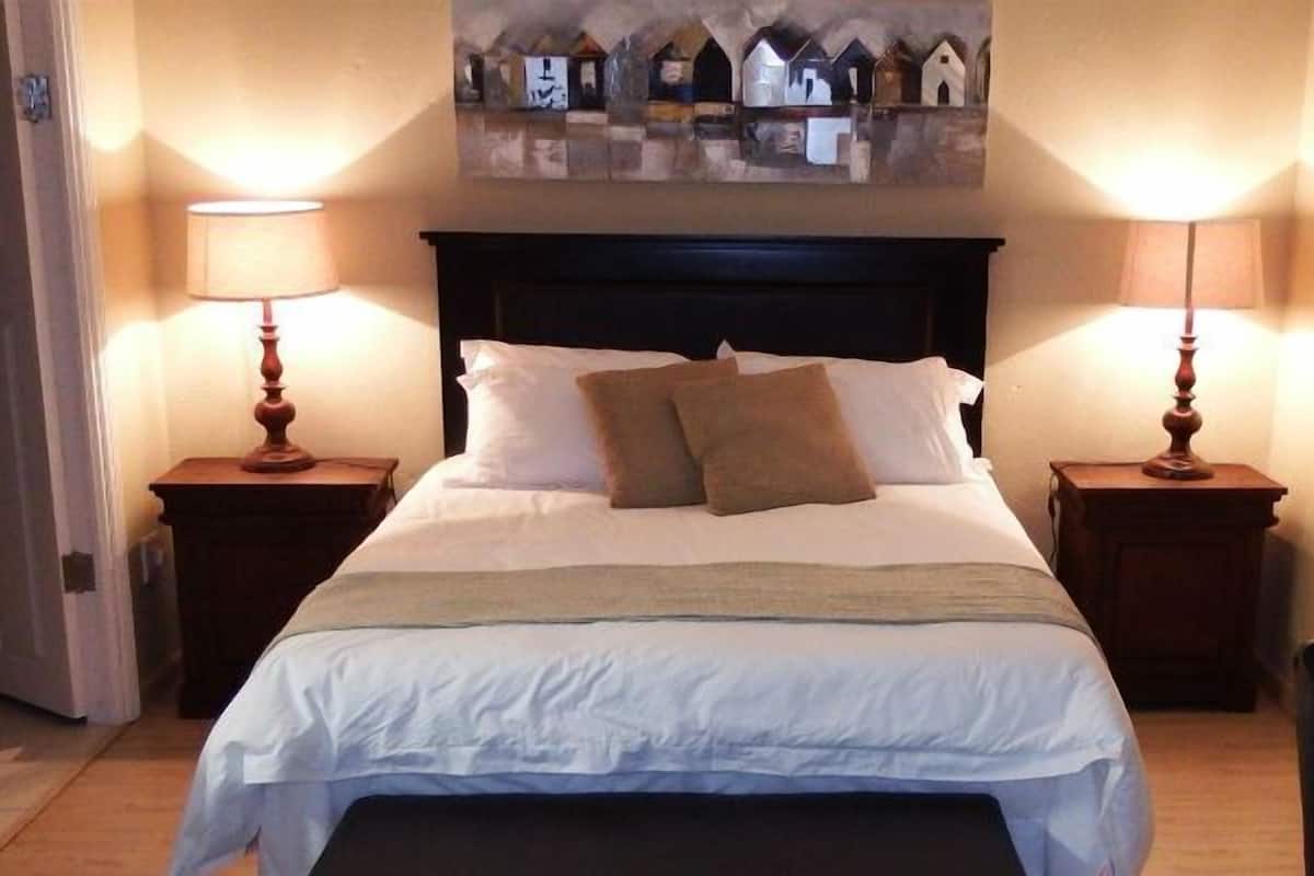 A hotel room with a large bed, two bedside tables with lamps, a painting above the bed, and a chair in the corner.