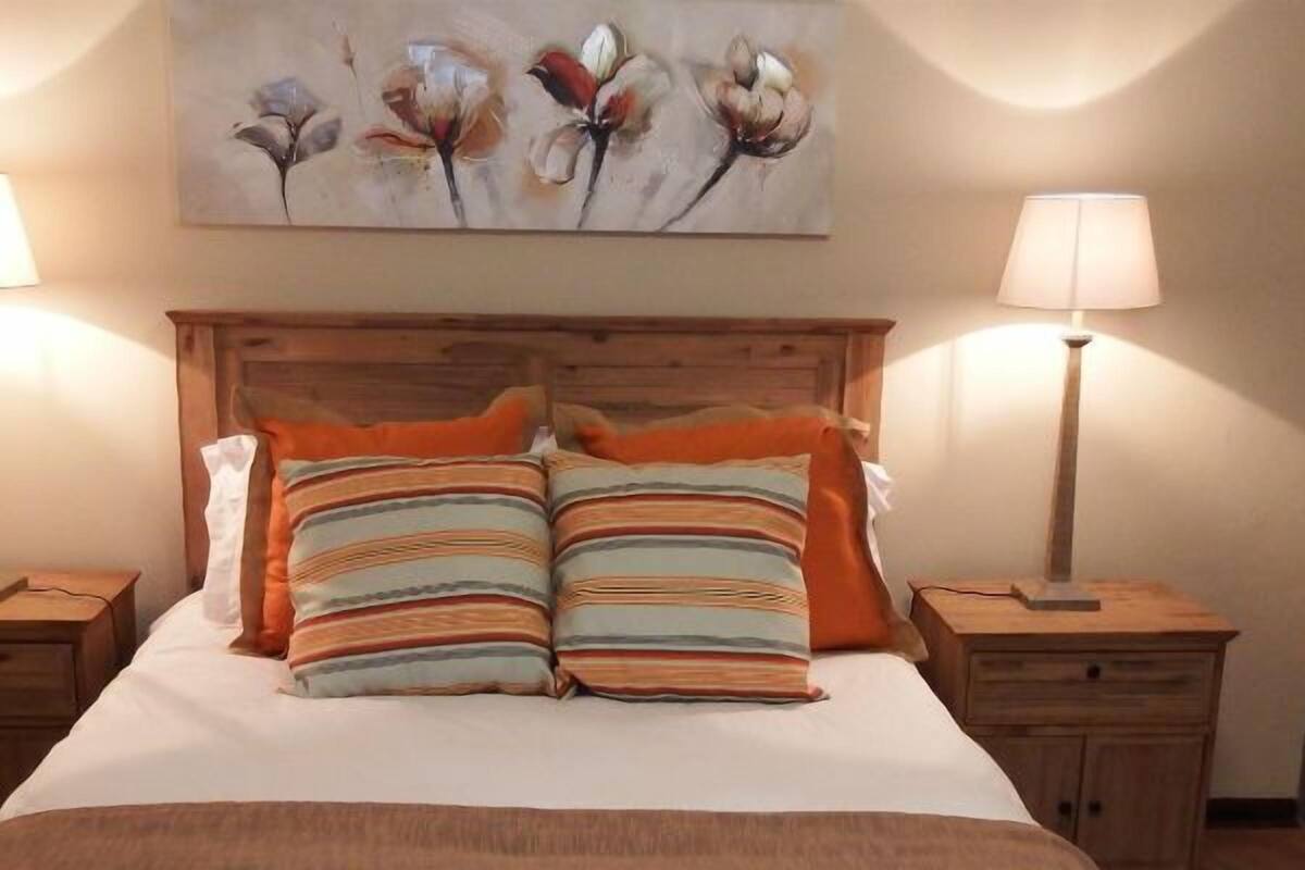 A neatly made bed with striped pillows, two bedside tables with lamps, and a floral painting above the bed.