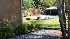 A pool area with a stone bench, surrounded by a well-maintained lawn and various plants. - 85 Ehmke (Mbombela)