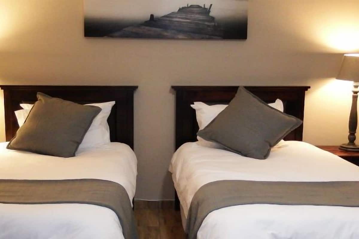A hotel room with two single beds, each with a wooden headboard and a bedside table with a lamp.