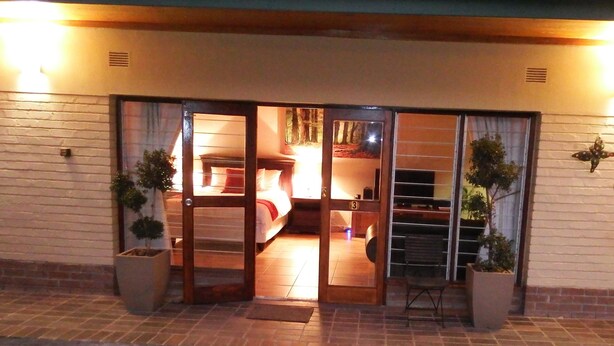A hotel entrance with a glass door leading to a room with a bed and a TV. There are potted plants outside the door. - 85 Ehmke (Mbombela)