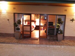Entrada de hotel con puerta de vidrio que da a una habitación con cama y televisión. Hay plantas en macetas afuera de la puerta.