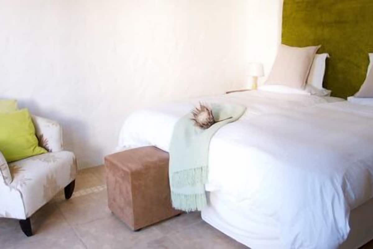 Une chambre à coucher avec un lit, une chaise, une table de chevet et une lampe.