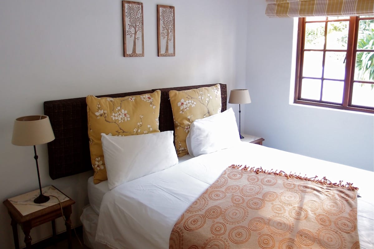 Une chambre à coucher comprenant un lit, deux lampes de chevet, une fenêtre donnant sur un paysage verdoyant et deux éléments de décoration fixés au mur.